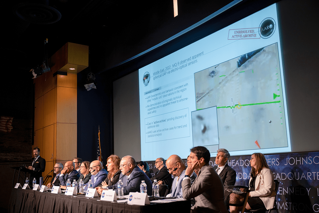 a group of experts sitting at a panel table with a projection behind them